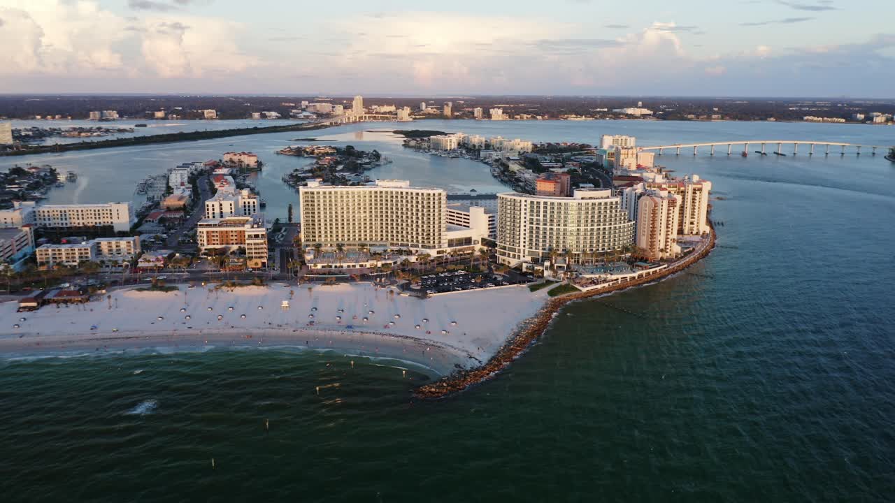 High-rise beachfront hotels line a sandy shoreline with calm turquoise waters, while coastal waterways and nearby residential islands stretch into the distance