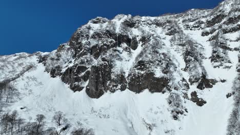 ascending shot flying up snow covered mountain cliff face, blue sky winter day