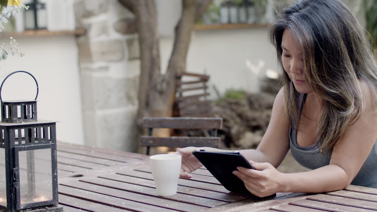 Medium shot of girl sitting at table in outdoor cafe with tablet