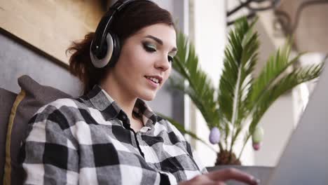 Close-up-footage-of-beautiful,-cheergul,-brunette-girl-in-plaid-shirt.-Happy-girl,-chatting-with-someone-using-a-laptop.-Headphones.-Indoors