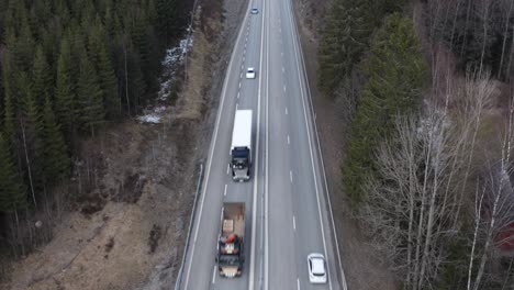 drone shot of highway in sweden running through forest, panning upwards to sky revealing forest, trucks and cars driving by