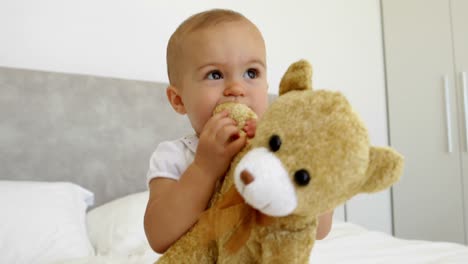 niña linda jugando con un oso de peluche en la cama