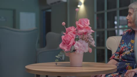 Seated-before-a-vibrant-pink-bouquet,-elderly-woman-engages-in-conversation