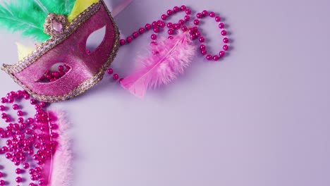 video of pink masquerade mask with feathers and mardi gras beads on lilac background with copy space