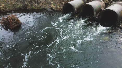 flying over the reservoir towards the concrete sewer pipes. streams of water flow through concrete pipes. polluted body of water in the park.