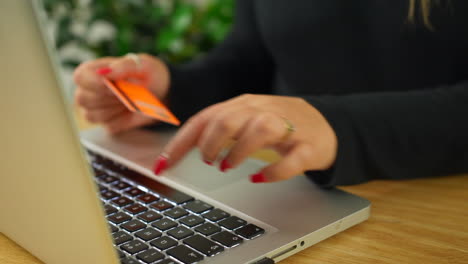 una mujer rubia irreconocible pagando en línea usando una tarjeta de crédito y una computadora portátil
