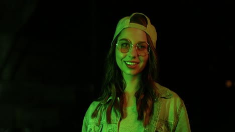 teenager caucasian girl with glasses and cap smiling and looking at camera outdoors at night