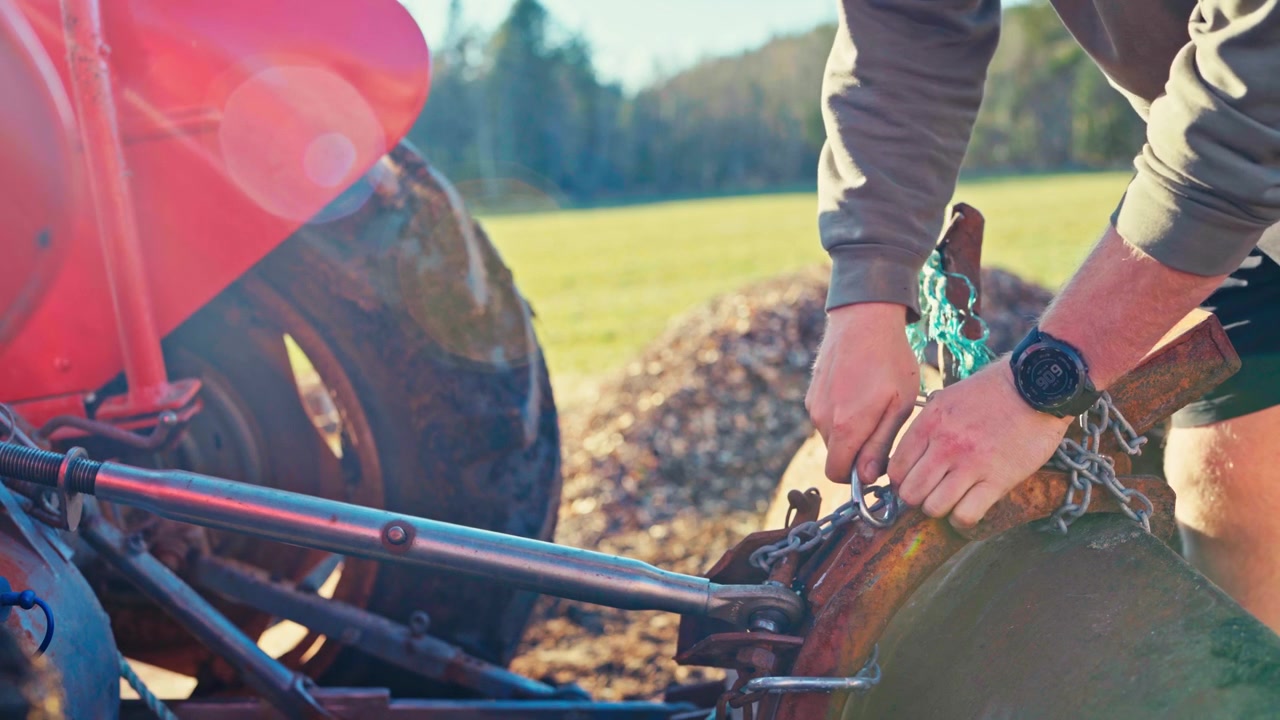 Man Uses A Heavy-Duty Chain And Rigging Setup To Attach Loader Bucket To A Vintage Tractor. Close-up Shot