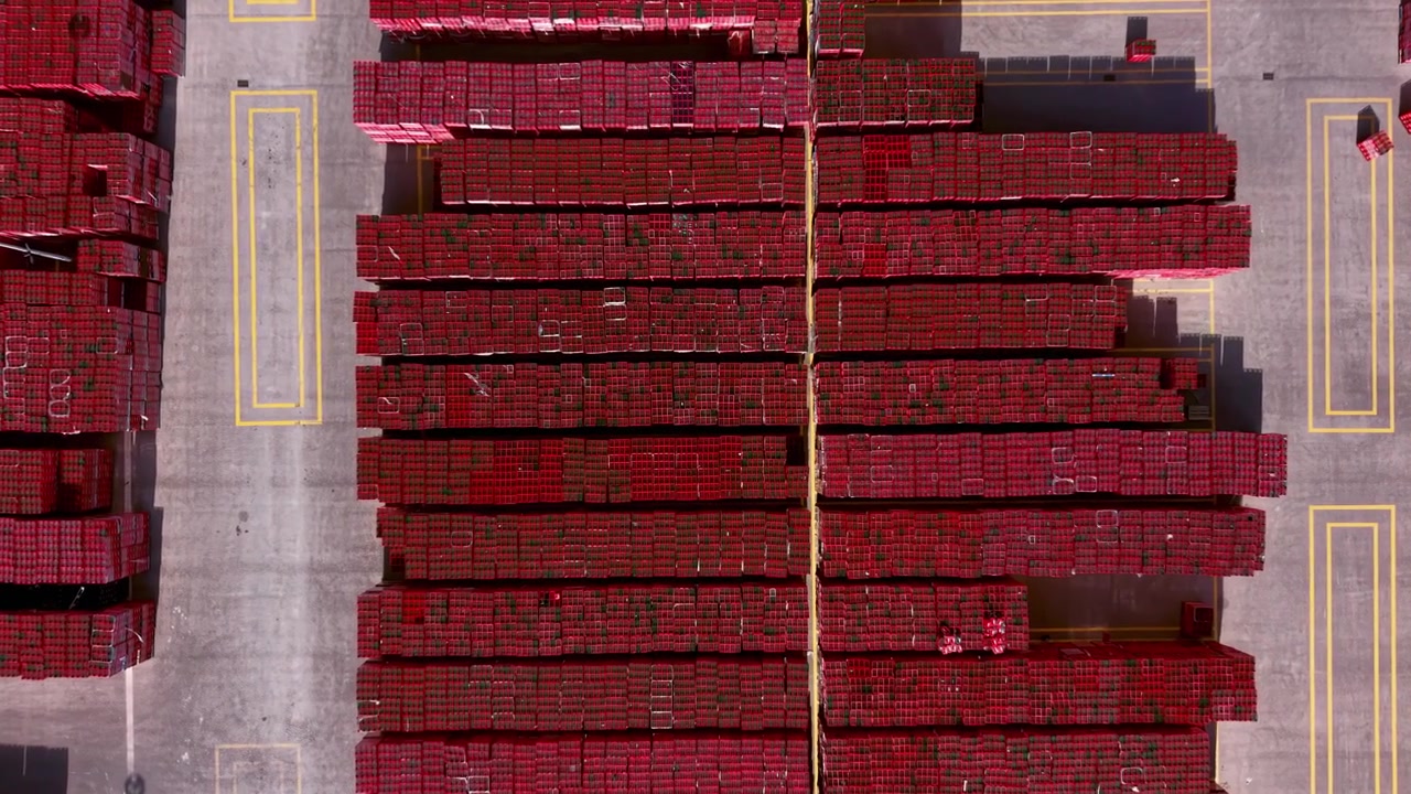 Vista dall'alto di enormi pile di casse rosse per bevande disposte in file su un piazzale in cemento marcato di un centro di distribuzione con linee gialle dipinte.