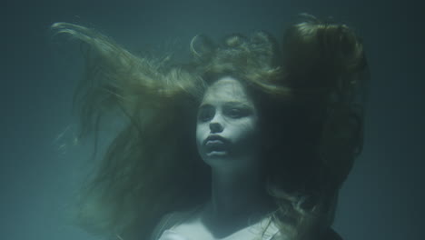 closeup of a beautiful girl with red hair in a white dress froze under water