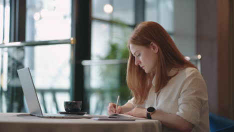 La-Mujer-Está-Trabajando-En-Casa-Escribiendo-En-Un-Cuaderno-Y-Viendo-Una-Conferencia-En-Una-Computadora-Portátil-Sobre-Educación-En-Línea-Sobre-Un-Trabajo-Remoto