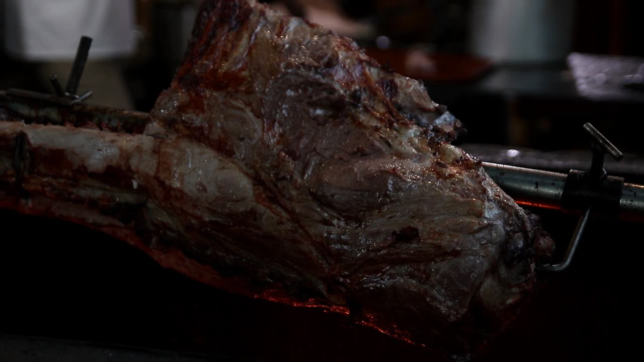 pieza entera de carne fresca y jugosa asada en un antiguo pincho de metal giratorio en un asador con llama abierta