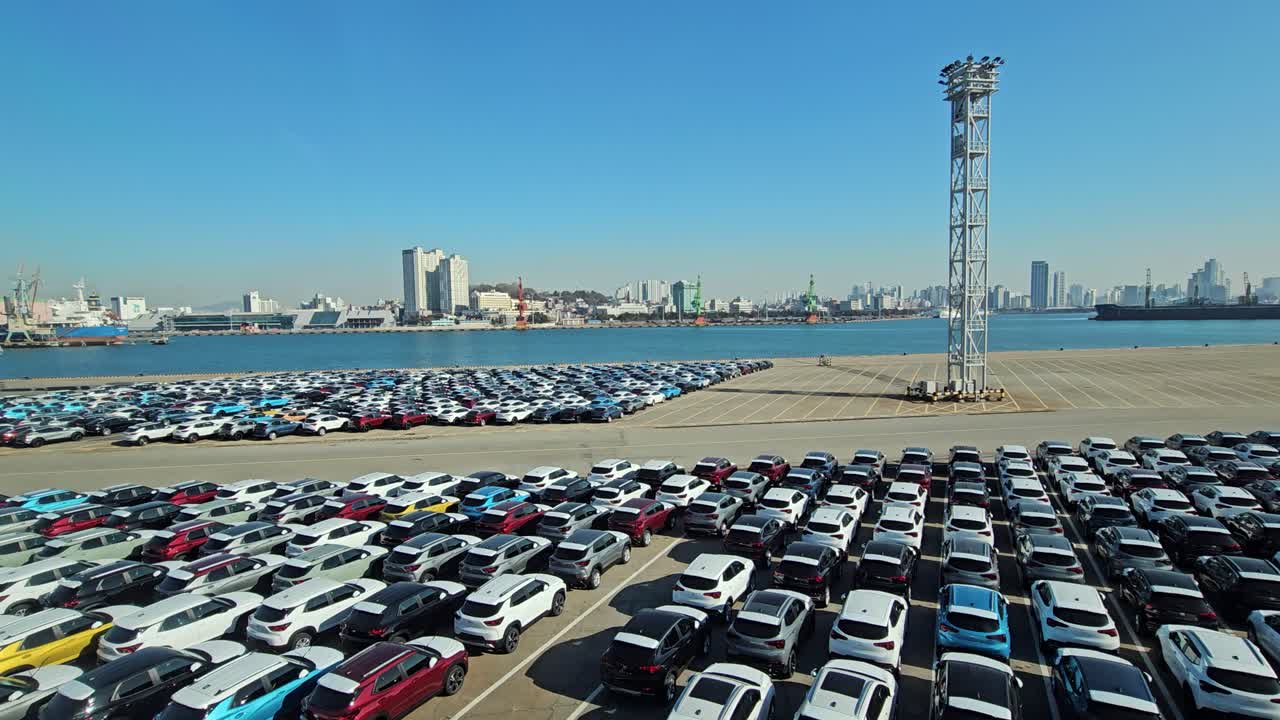 A vast parking area at Wolmi Port, Incheon, filled with cars in rows, overlooks the city skyline and docked ships under a bright blue sky - dolly drone shot