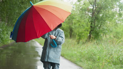 child twirls umbrella in hands in park boy plays with multicolored parasol spending time in garden