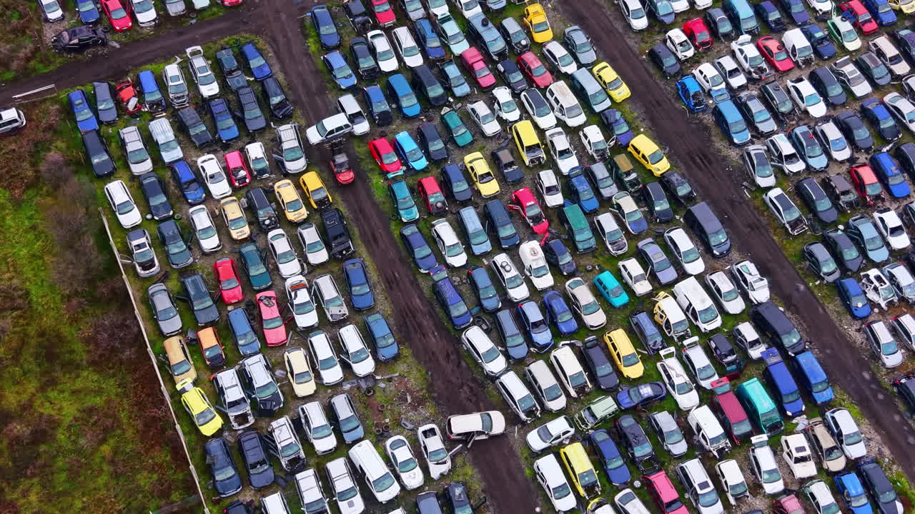 Sfasciacarrozze in un campo aperto che mostra una varietà di veicoli colorati parcheggiati molto vicini sotto un cielo sereno durante il giorno.