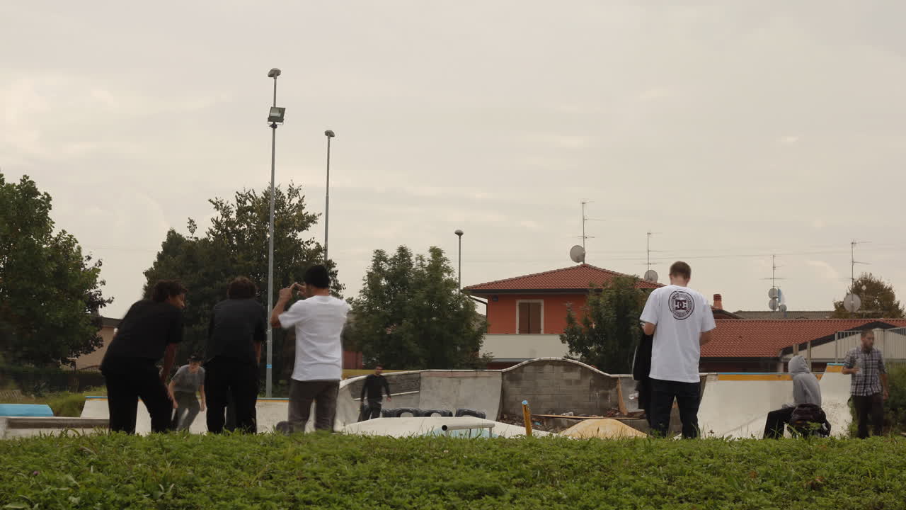 Skaters hang out in a suburban park under cloudy skies, blending urban youth culture with a quiet residential backdrop