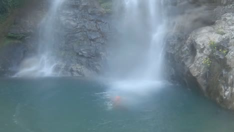 young man jumping in waterfall from cliff at morning from flat angle