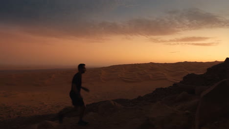 man running up a rocky hill in the desert at sunset