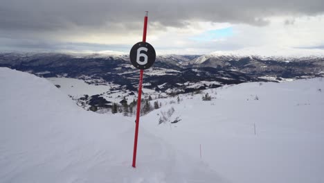 Personas-En-Snowboard-Distante-Por-Un-Sendero-Negro-En-El-Famoso-Destino-De-Esquí---Moviéndose-Hacia-Atrás-Mostrando-La-Pista-De-Esquí-Y-Una-Vista-Panorámica-De-Las-Montañas-Cubiertas-De-Nieve