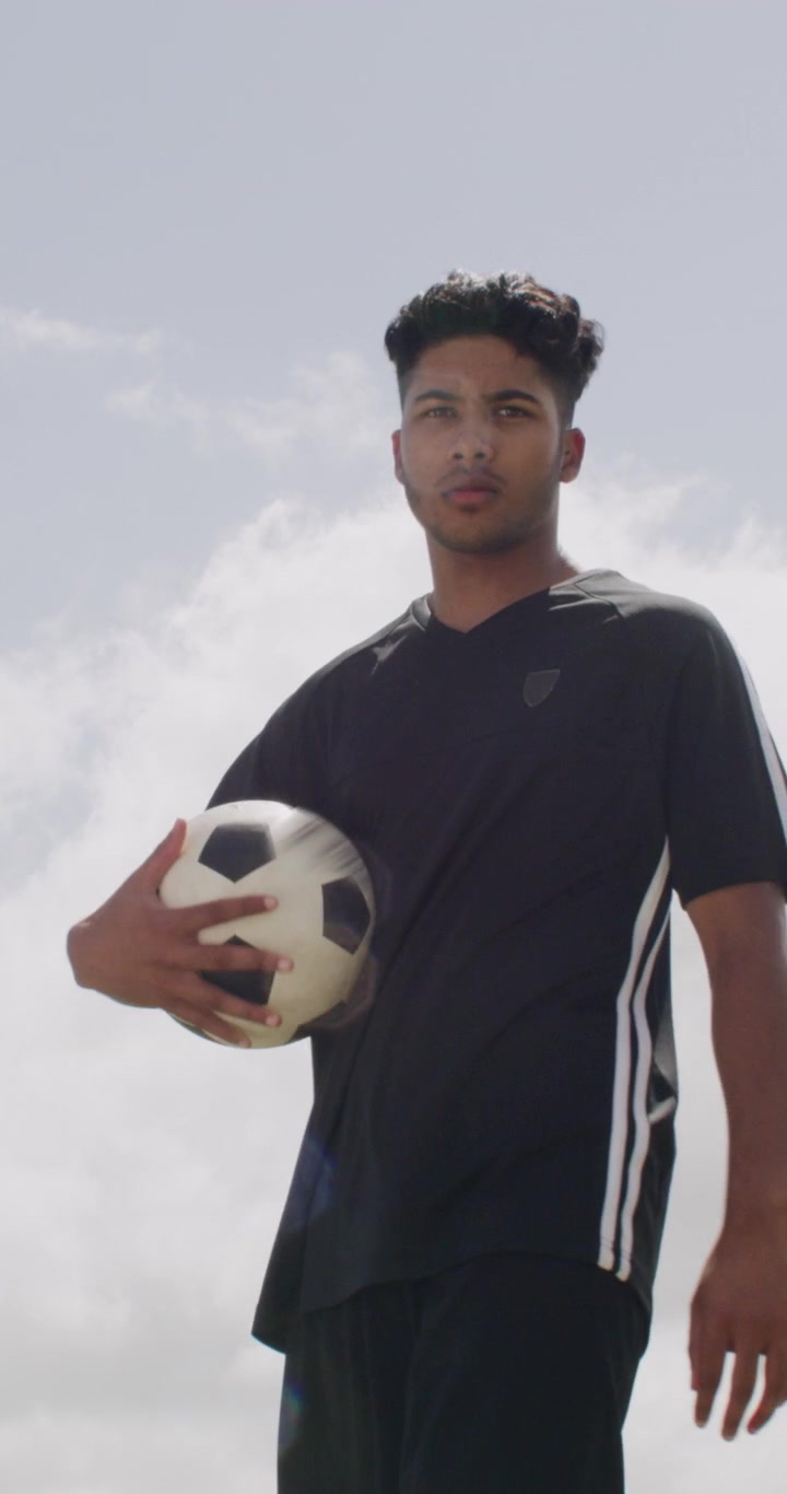 Joven futbolista atrapando un balón contra un cielo nublado