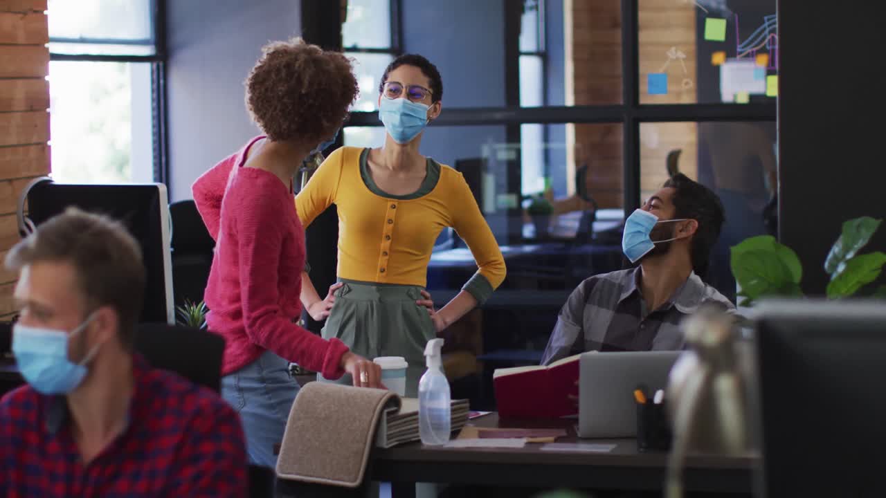 Diverse colleagues wearing face masks discussing together at modern office