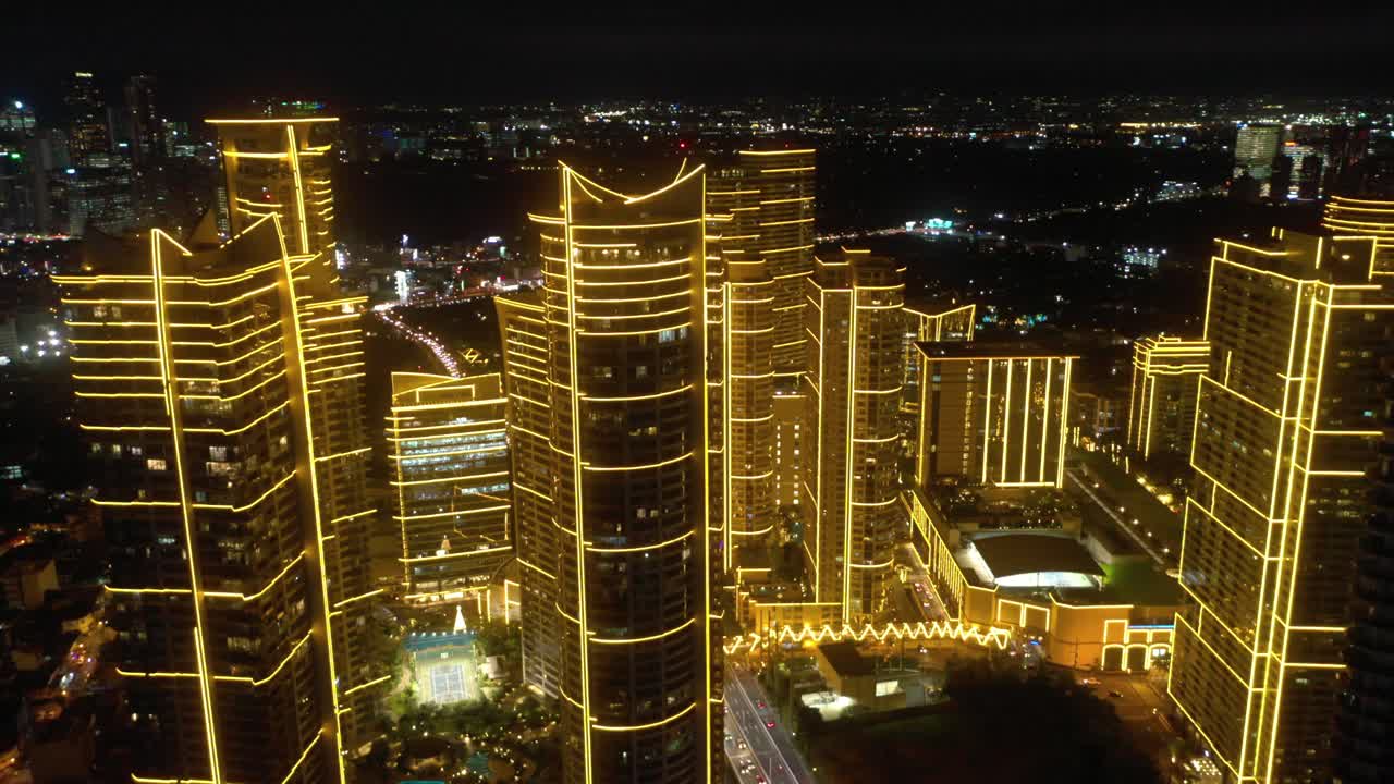 Aerial drone footage of Rockwell Center skyscrapers in Makati, Metro Manila, glowing with lights at night and surrounded by the vibrant energy of the city skyline.