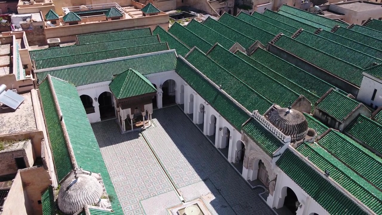 Prospettiva aerea media da drone che mostra il tradizionale padiglione del cortile interno, la cupola bianca del minareto e i tetti paralleli in tegole verdi della Moschea Al Quaraouiyine a Fez, Marocco