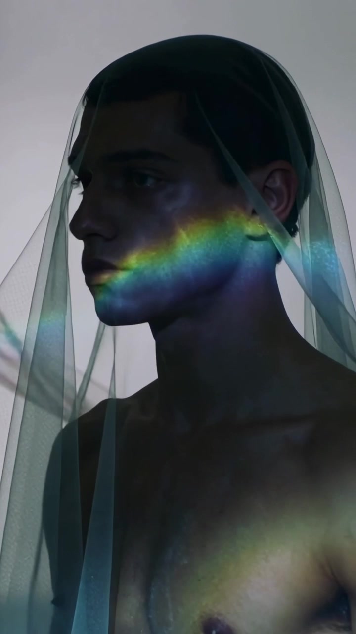 Video verticale: Modello maschile a torso nudo che reagisce alla luce del prisma, inclinando la testa in studio, con un velo trasparente.