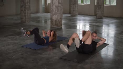 atletas de fitness mujer y hombre vestidos con ropa deportiva oscura realizan un ejercicio levantando las rodillas hasta el pecho para los músculos abdominales, en la alfombra en el estudio loft . en el interior. entrenamiento, deporte, cámara lenta