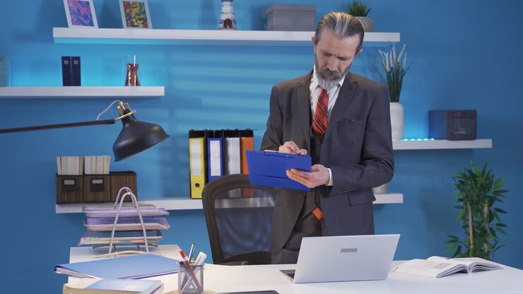 Uomo d'affari maturo lavora al laptop in ufficio prendendo appunti.