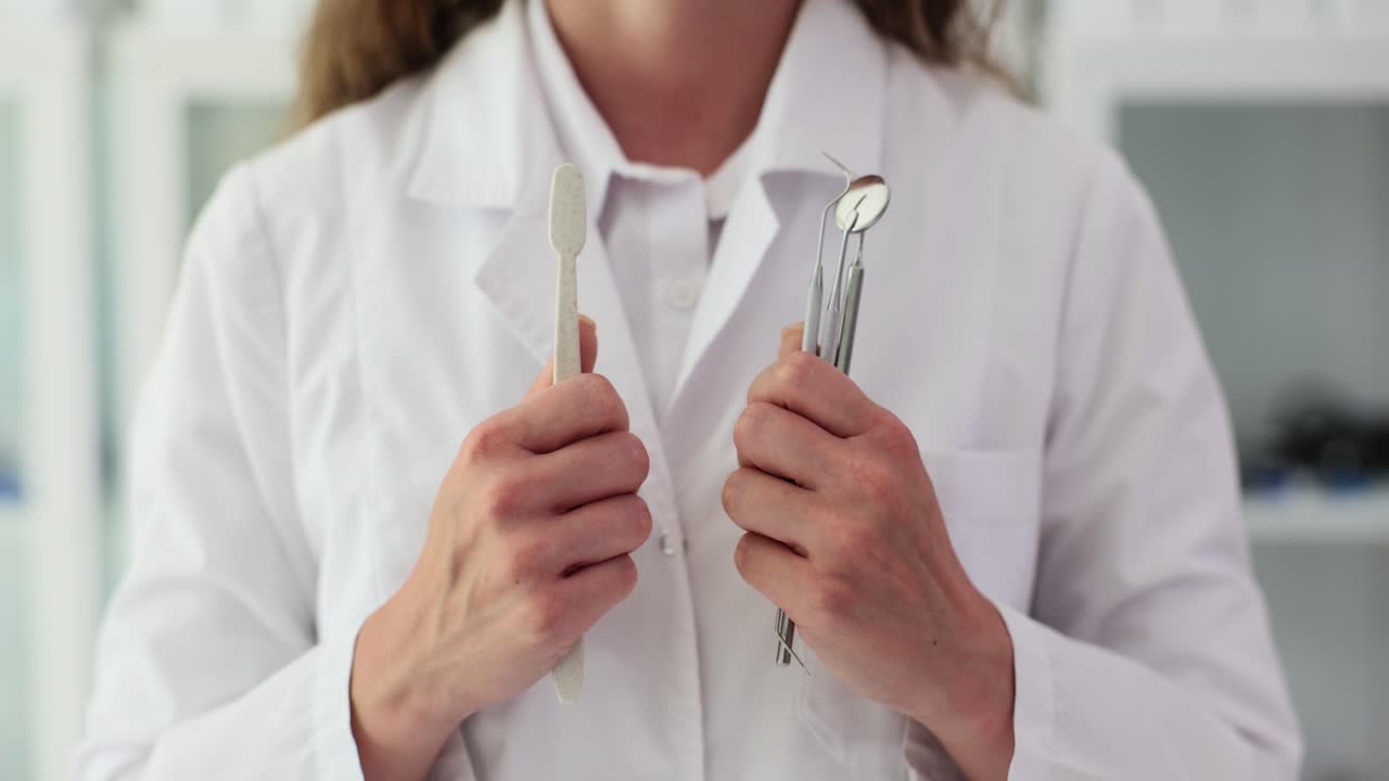 Person in lab coat holding toothbrush and dental tools