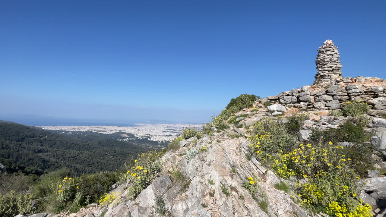 Cairn di pietre sulla cima di una montagna con vista su Atene, inquadratura grandangolare che si sposta a destra rivelando il cairn