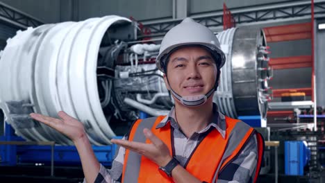 close up of asian male engineer with safety helmet smiling and pointing to side while standing with airplane engine maintenance conducted, analytics checking the turbine