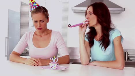 woman blowing party horns beside her upset friend in kitchen