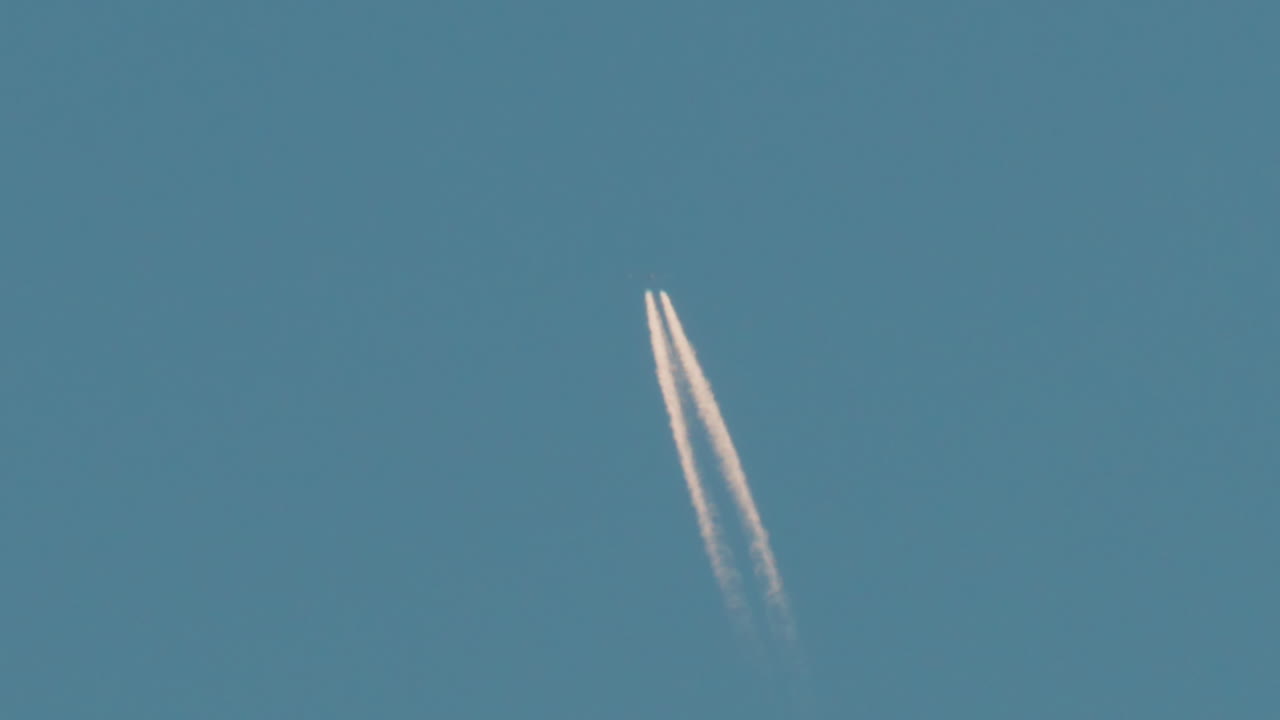 Airplane flying high above leaving long contrails in a clear blue sky
