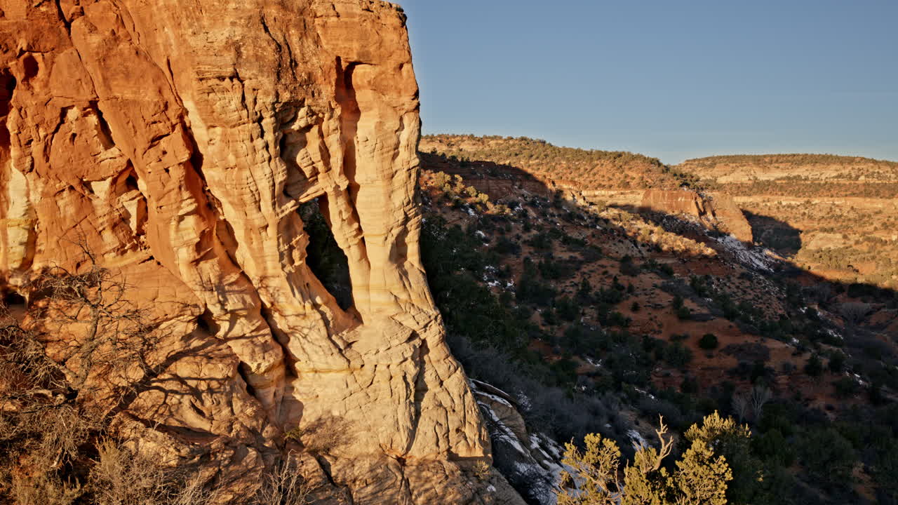 Drone pans across a rugged red rock landscape, focusing on a striking natural arch at dawn.