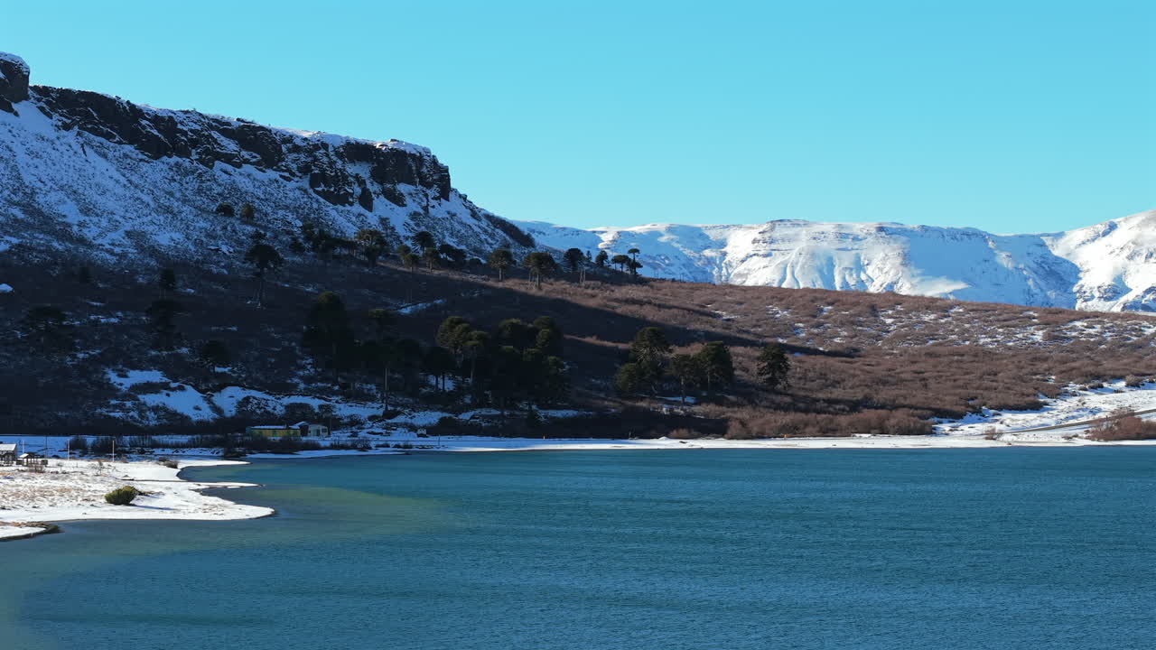 A breathtaking aerial drone shot of the winter landscape in Caviahue, Patagonia, Argentina. The view captures the snow-covered Andes mountains and the clear blue lake