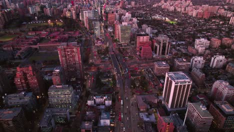 Aerial-Drone-Fly-Above-Santiago-City-Chile-Escuela-Militar-Metro-Station-at-Dusk-Pink-Sunset,-Traffic-at-Main-Avenue