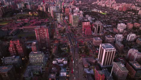 Abejón-Aéreo-Que-Vuela-Sobre-La-Estación-De-Metro-Militar-De-La-Escuela-De-La-Ciudad-De-Santiago-Chile-Al-Atardecer-Rosa,-Tráfico-En-La-Avenida-Principal