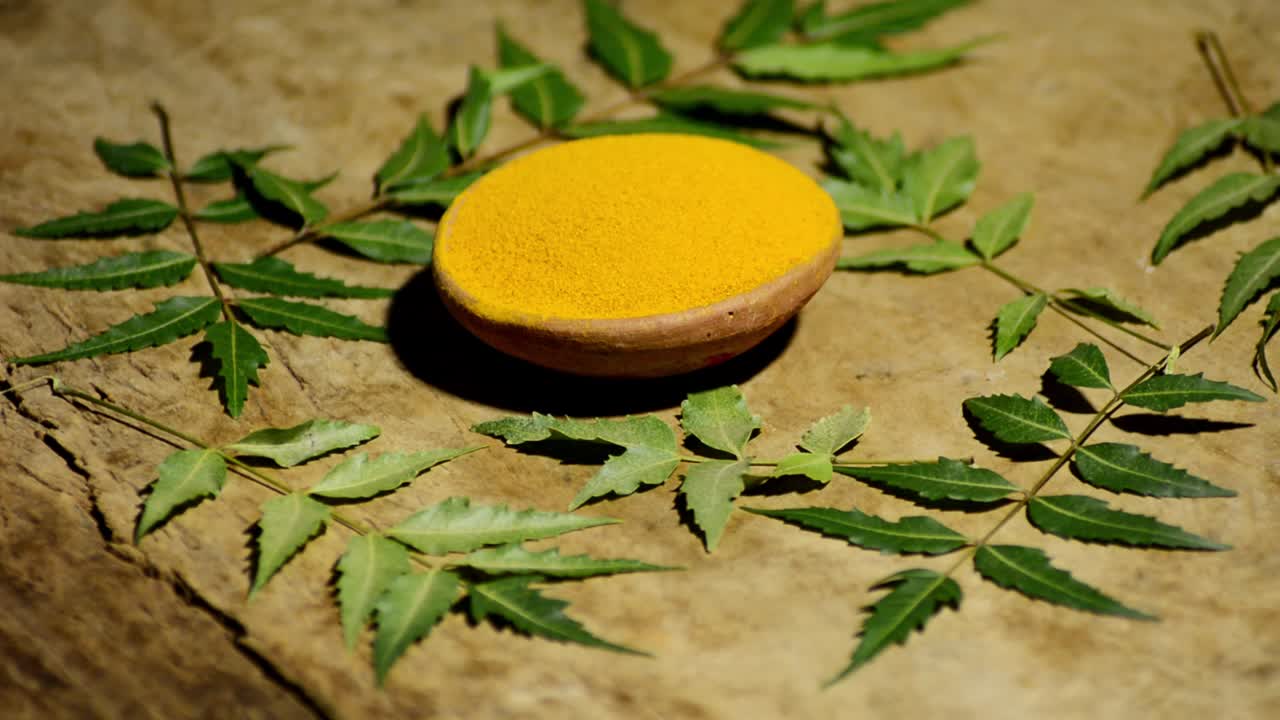 Medicinal turmeric powder with neem leaves over wood background