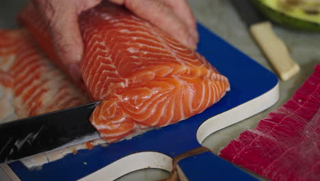 fresh raw salmon fillet on cutting board being prepared for sushi or sashimi in soft light, knife cuts through meat in slow motion