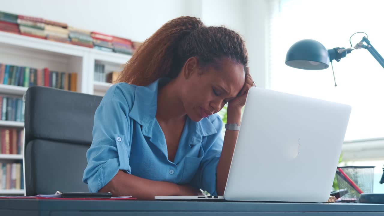 joven mujer afroamericana infeliz mira la computadora portátil se sienta en la mesa de la oficina