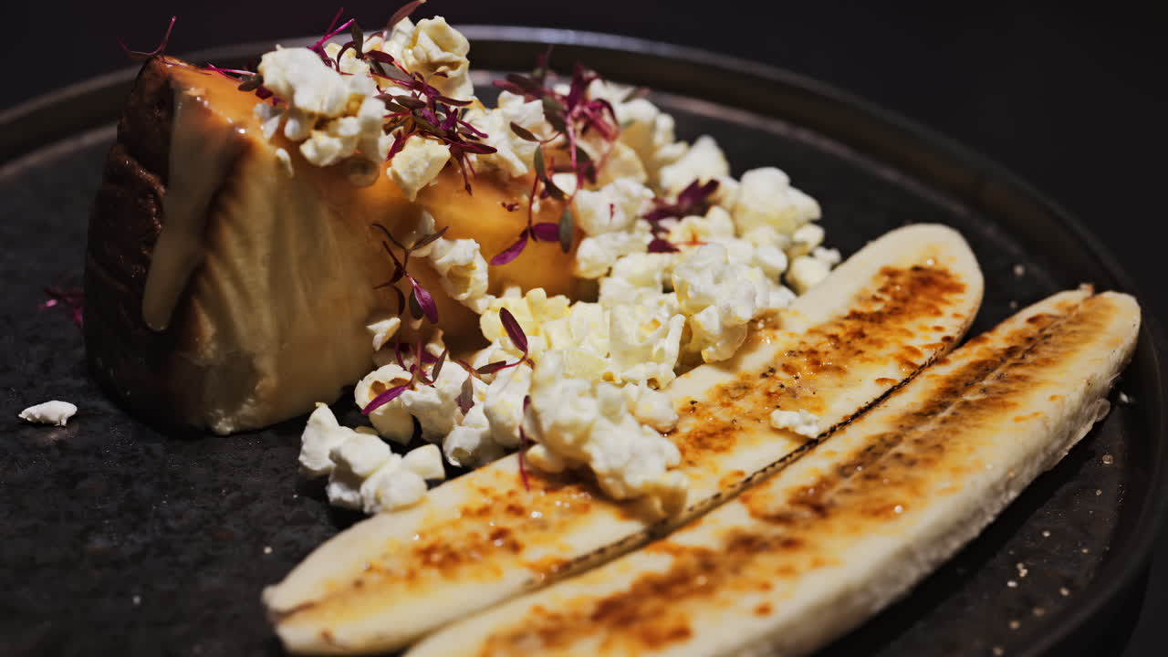 Close up of a cheesecake with a banana split and caramelised popcorn on a black plate at a restaurant