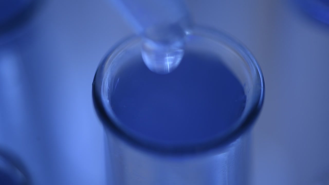 Primo piano di un contagocce che aggiunge liquido trasparente a una provetta blu