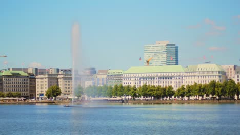 4k slow motion: giant water fountain in the middle of a lake in the centre of hamburg, germany. camera panning with houses in the background