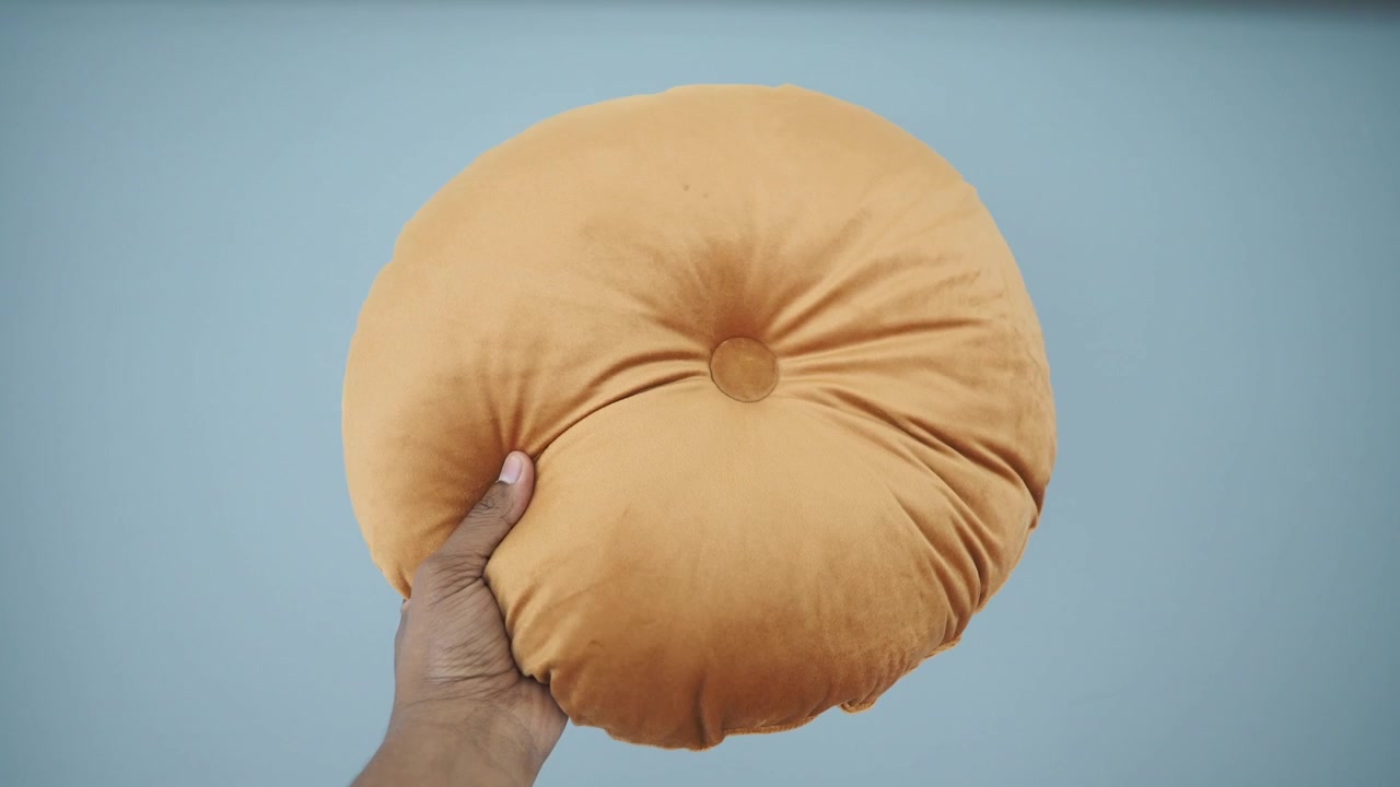 Mano che tiene un cuscino decorativo rotondo in velluto giallo