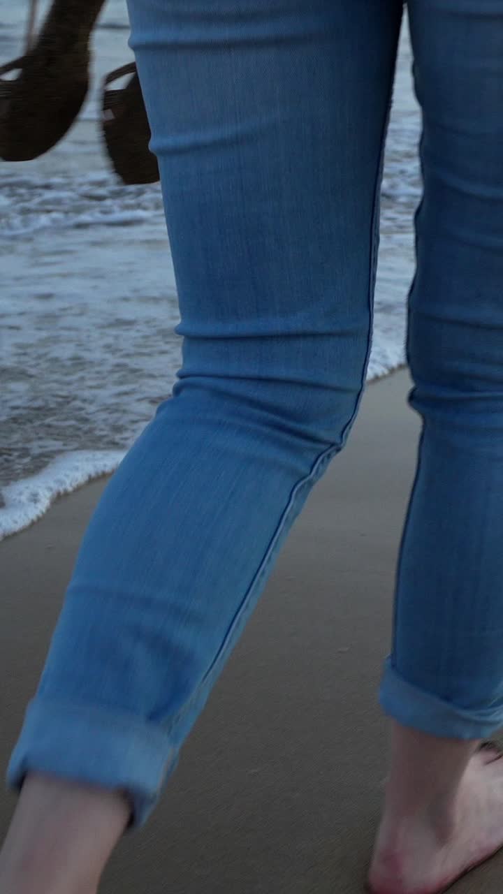 Woman's bare feet walking at the water's edge on a sandy beach at sunset