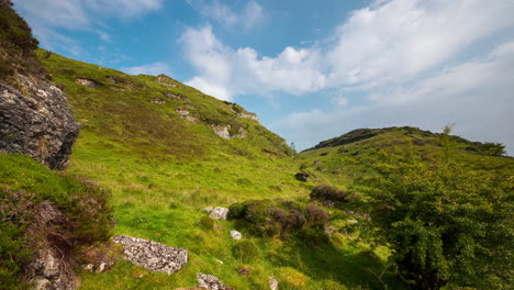 panorama motion time lapse of rural landscape with large rocks in grass field hillside during a cloudy summer day in ireland