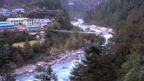 Un-Río-Glaciar-Que-Serpentea-A-Través-De-Un-Valle-Bordeado-Por-Montañas-Escarpadas-Con-Un-Puente-Colgante-Sobre-El-Río