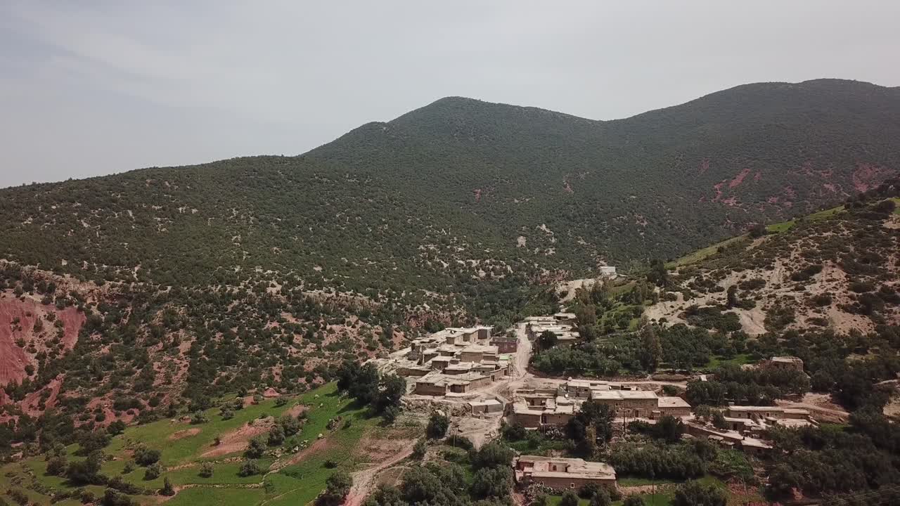 Ampia ripresa aerea di un remoto villaggio berbero situato sui pendii rossi e accidentati delle montagne dell'Alto Atlante. Il filmato mette in risalto le texture geologiche, la terra rossa e gli insediamenti rurali nell'Africa settentrionale.
